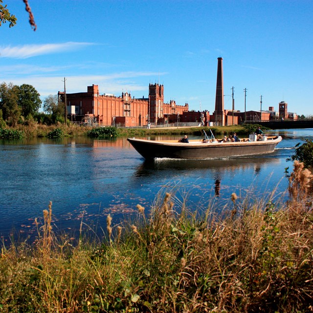 Tour boat going down canal with brick mill in background