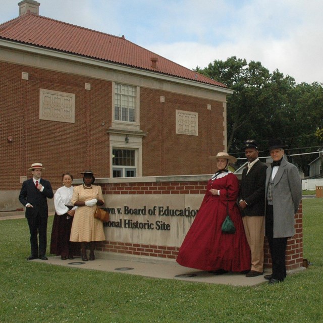 people in period dress stand in front of park sign