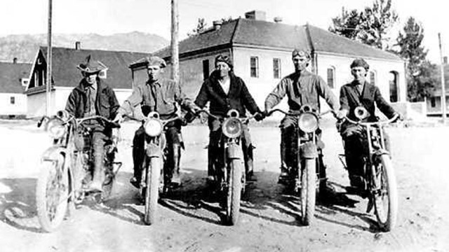 Four men on motorcycles in front of buildings. Motorcycle patrol at Yellowstone National Park. 1919