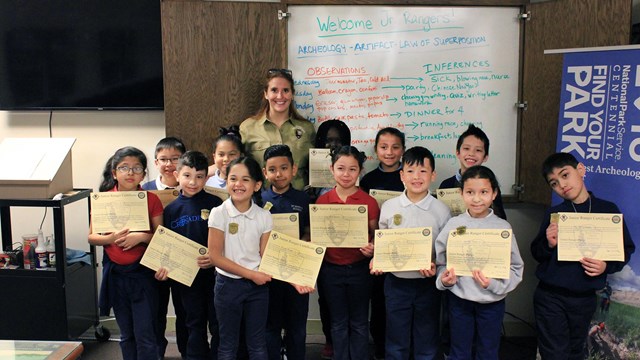 Group of elementary students displaying their junior ranger certificates in front of a whiteboard