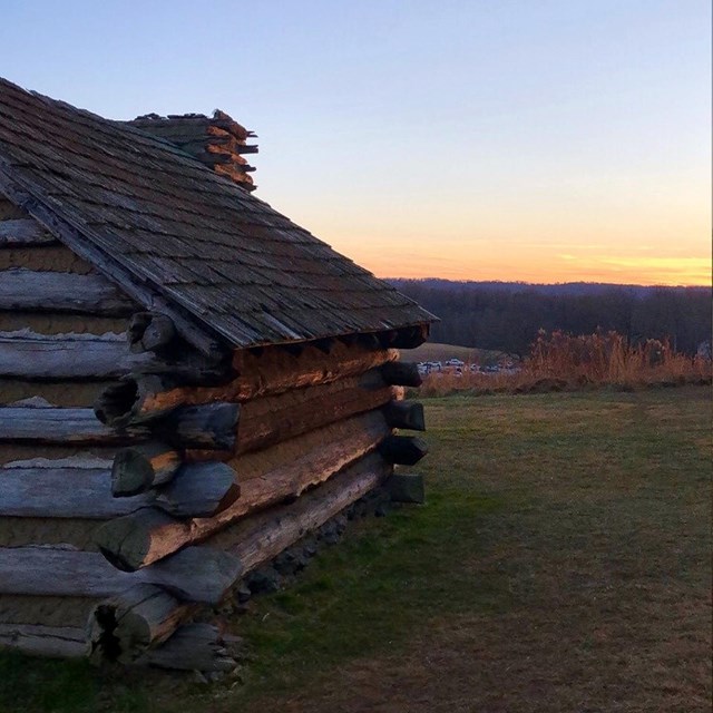 Log house stands in field at sunset