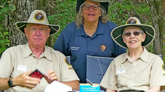 Three volunteers in uniform sit behind a desk smiling.