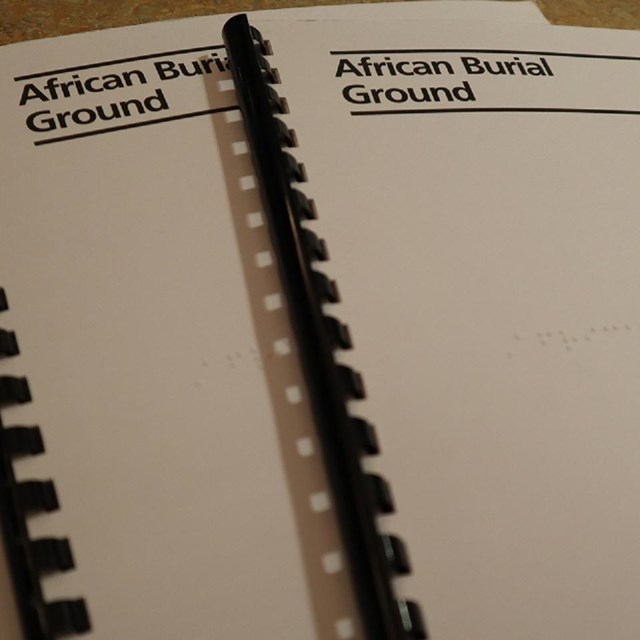 Three white Braille books that read African Burial Ground at the top left.
