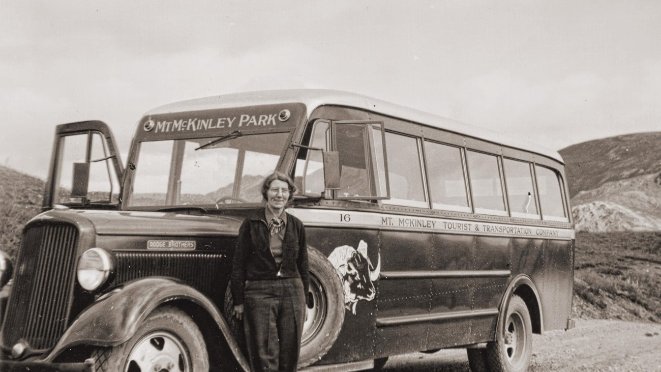 a woman standing near a bus on a dirt road