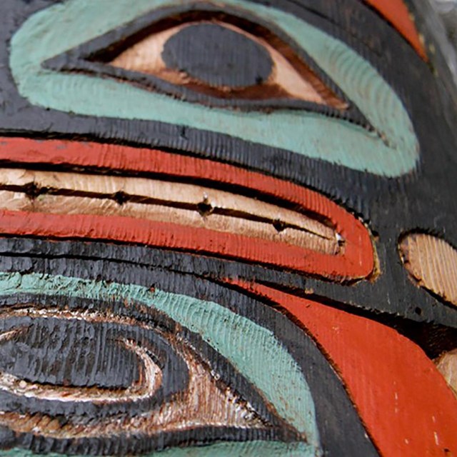 Close-up of totem pole carving. Two oval eyes and a mouth painted in primary colors.