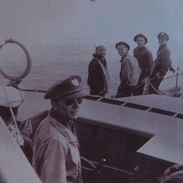 Black and white photo of five men on a boat on water. 