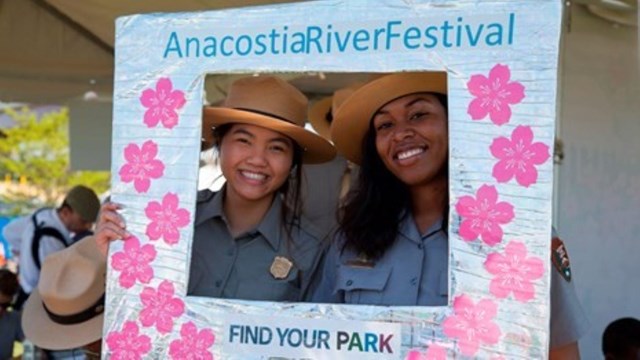 Two rangers stand behind an Anacostia River Festival sign