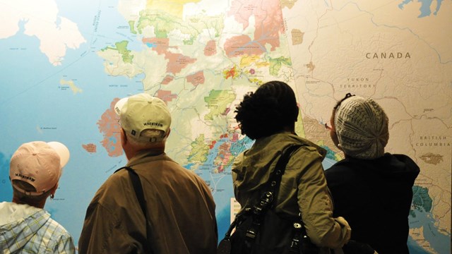 Indoors; group of four adults with back to camera, looking at lit up map.