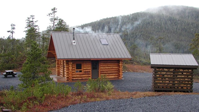Newly built log cabin on gravel driveway with foggy treed mountains in background.