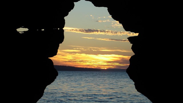 A orange and yellow sunset over lake Superior viewed through a sea cave archway
