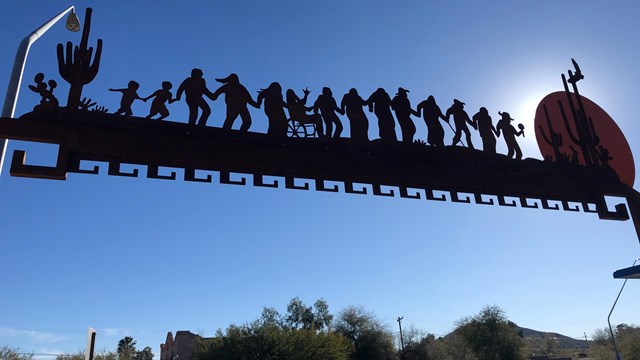 A silhouette of an metal archway sculpture depicting people holding hands in a line