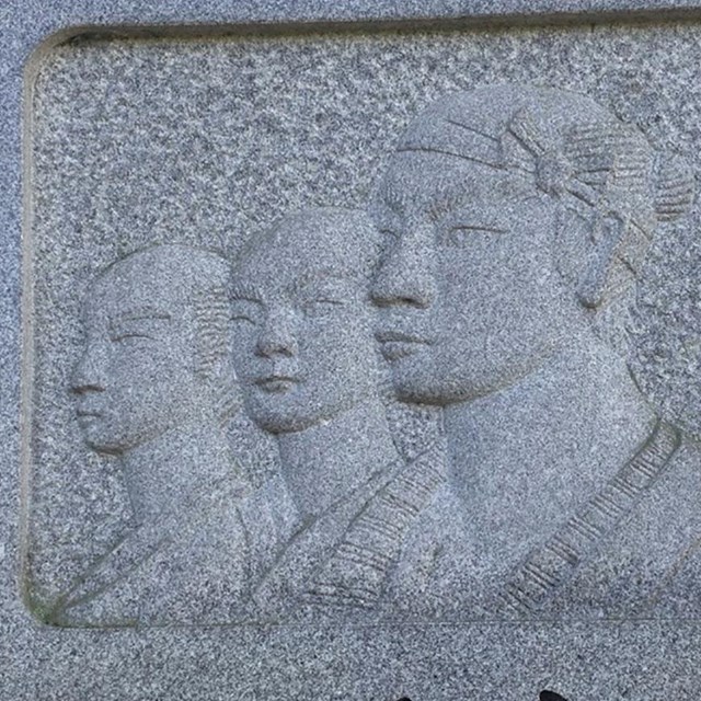 A stone monument with carvings of three men and writing in Japanese.