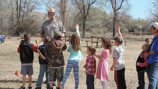 A group of young students in a line facing a ranger with their hands raised.