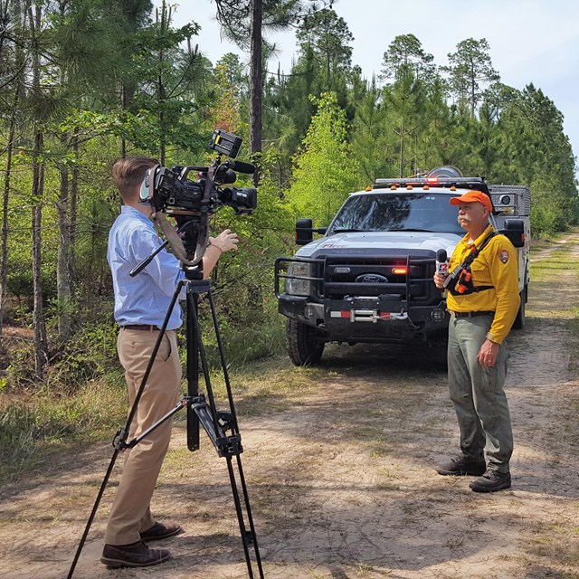 firefighter being interviewed on camera by a reporter, in front of a white truck