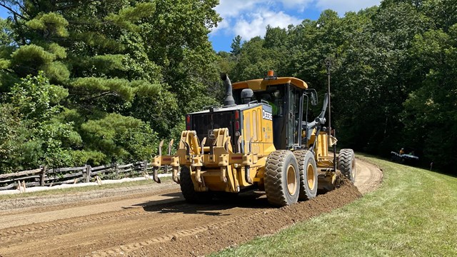 A yellow construction vehicle sits on an unpaved section of the Blue Ridge Parkway.