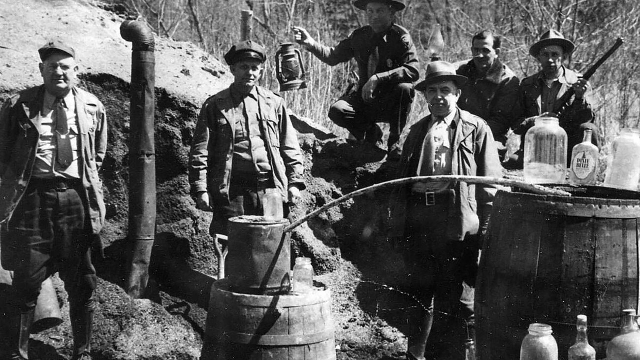 historic photo of moonshine still with law enforcement officers