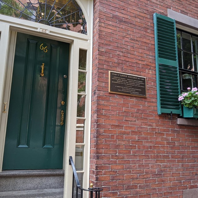 Brick townhouse with an arched entryway, a green door, and green shutters on the first flower window
