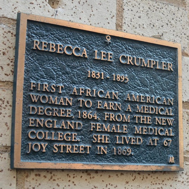 Stone wall of a building next to a black doorway. Plaque on wall about Rebecca Lee Crumpler.