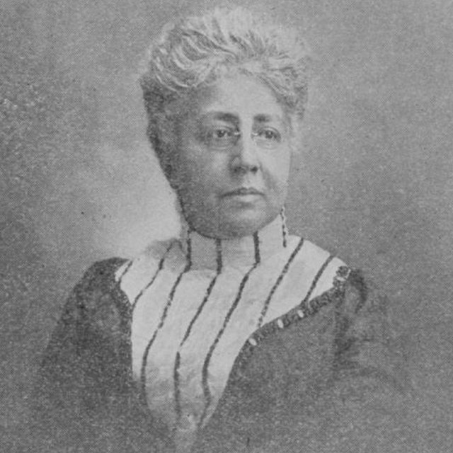 black and white print of a Black woman with short white hair, small glasses and a high-collared top