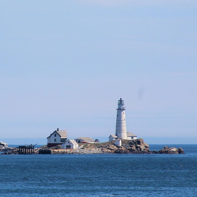 A small, rocky island with a lighthouse station, lighthouse, and other small white buildings.