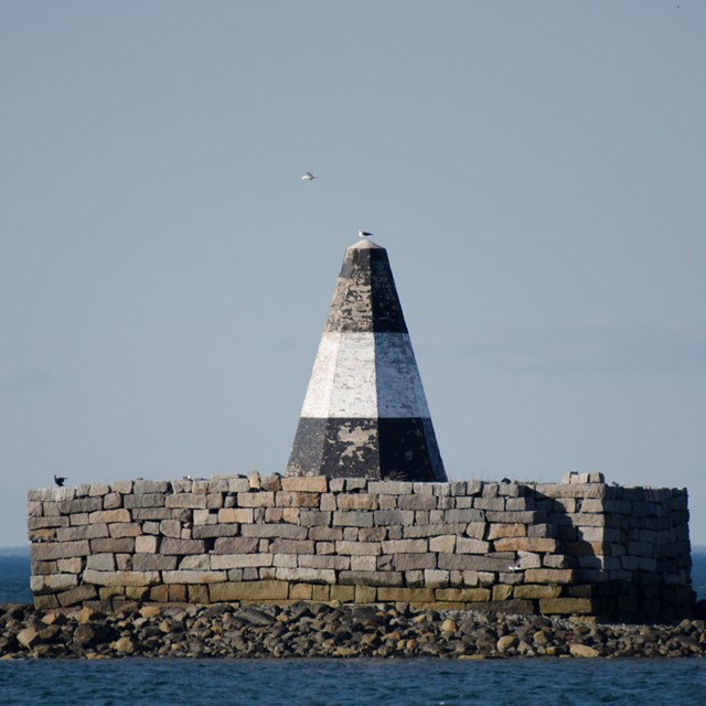 A large black and white cone-shaped marker on top of a brick stand on a tiny island.
