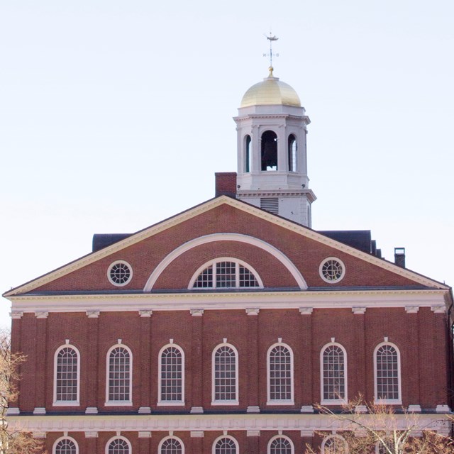 A view of brick Faneuil Hall with its white cupola with a gilt dome.