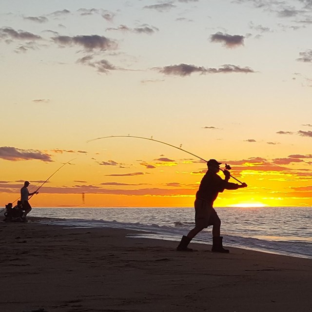 The silhouettes of fishermen are framed against a brilliant sunset.
