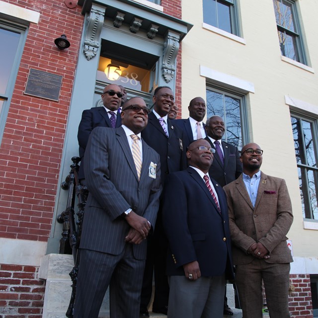 Members of Omega Psi Phi Fraternity, Inc. stand outside the Woodson Home