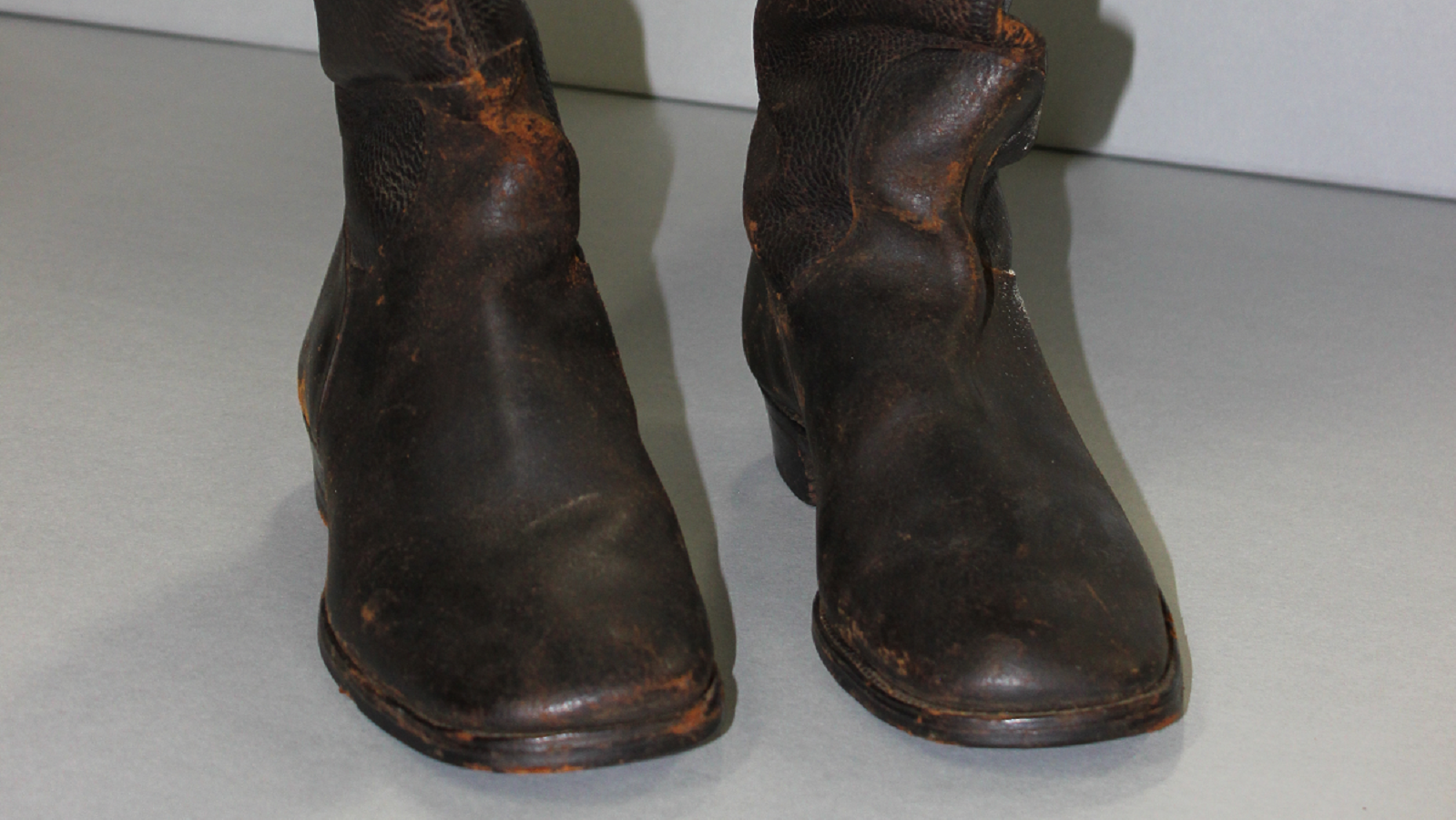 Old pair of brown, tall riding boots against a gray background. 