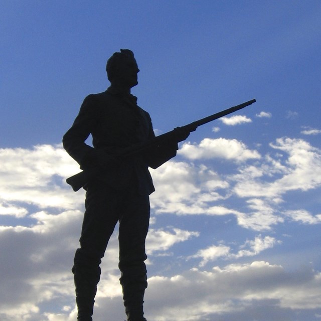 Backlit statue of man holding a rifle.