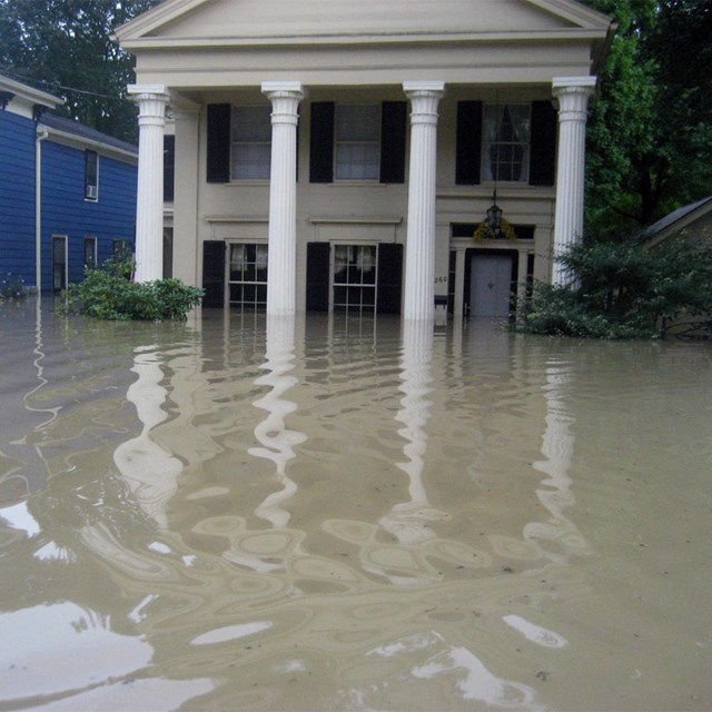 Murky water floods the first floor of an old house fronted by large white columns