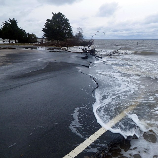 A paved parking area disappears into ocean waves and disintegrates