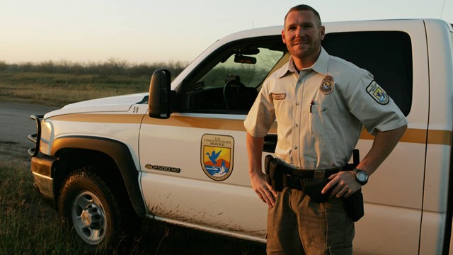 Fish and Wildlife Service employee standing by a USFWS vehicle.