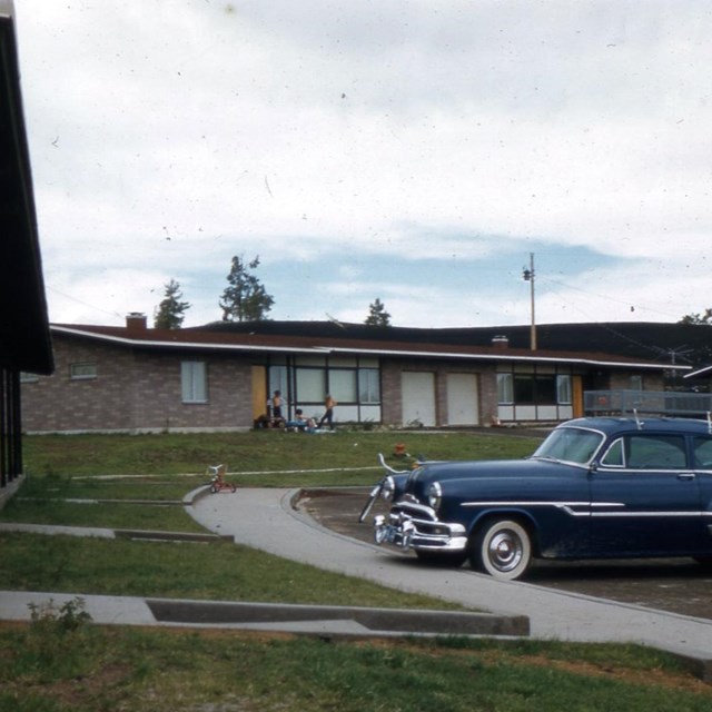 several long brick buildings with lawns and a 1950s era car parked in front