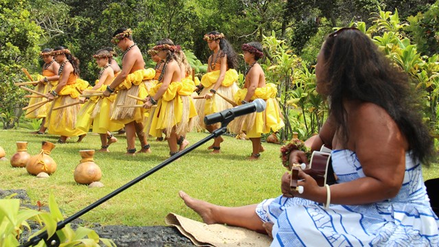 Woman singing to a line of hula dancers