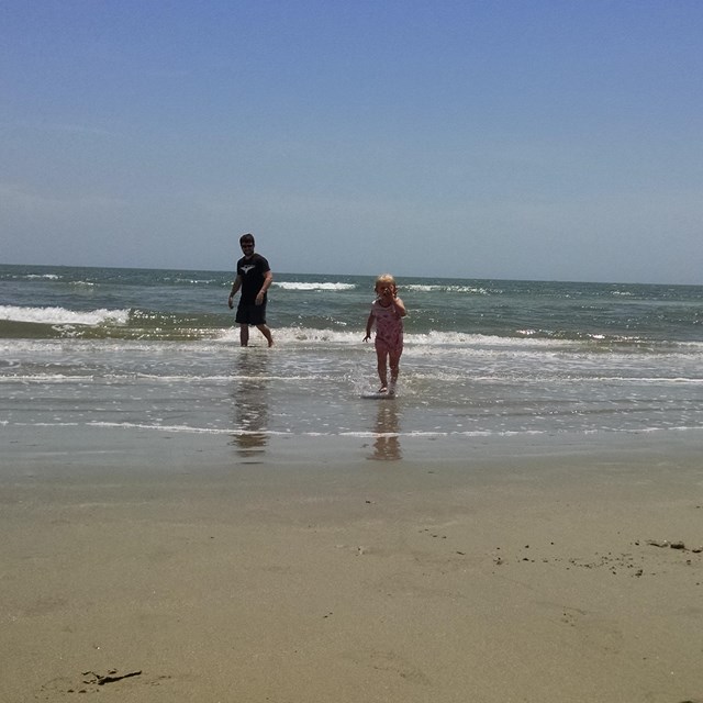 Man and young girl play in the surf on the beach