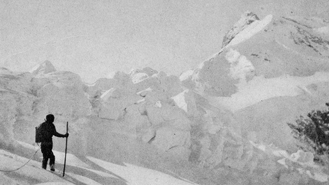 a historic photo of a man standing on a snow overed mountain