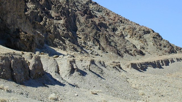 A long, raised bed ledge of rock runs along a desert mountain. 