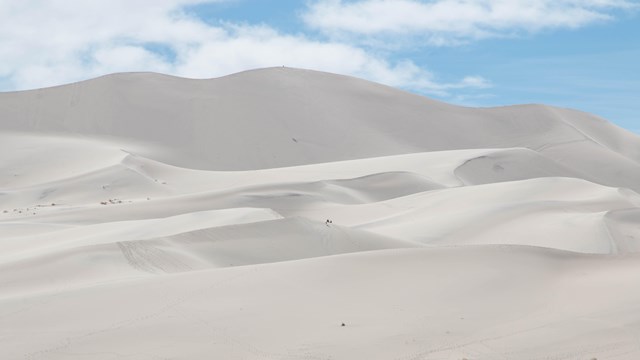 A large towering sand dune under a blue sky with scattered clouds. 