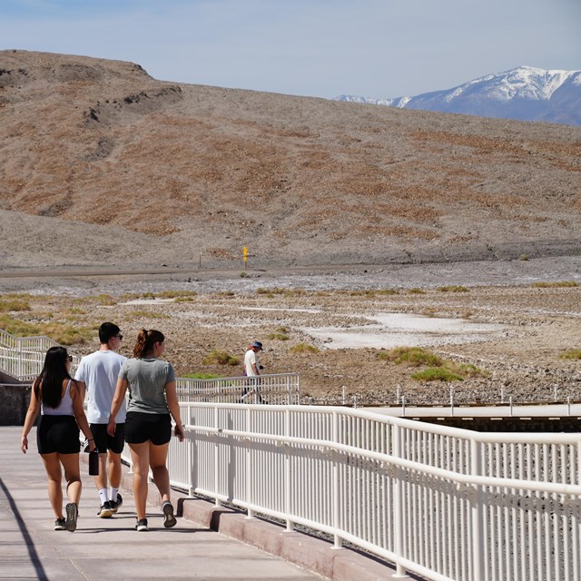 Group of 3 people looking out at the view as they walk down a ramp at Badwater Basin.