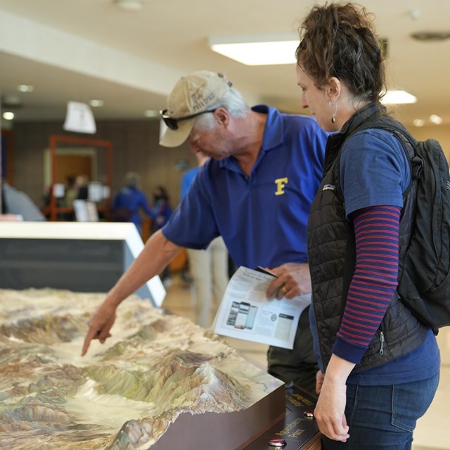 A couple is standing next to a tactile map of the park and the man is pointing out specific areas.