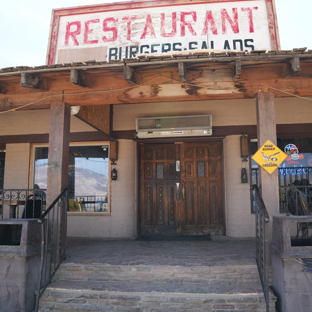 Front of restaurant with wooden door, stairs, and various signs