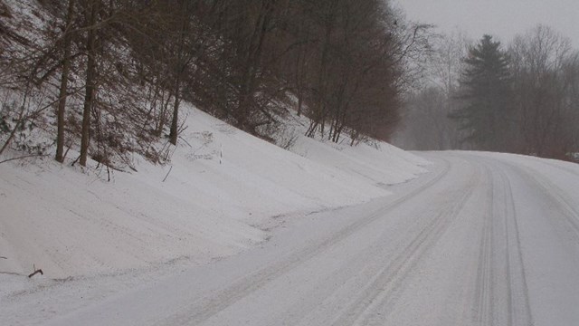 A snow-covered road with snow drifts on the left side.