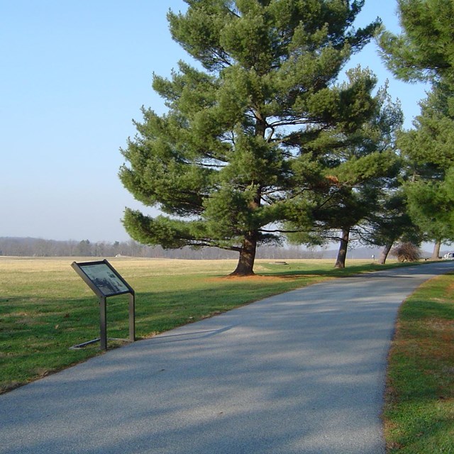 Photo of a paved trail at Eisenhower Farm overlooking an open filed with a informative sign.