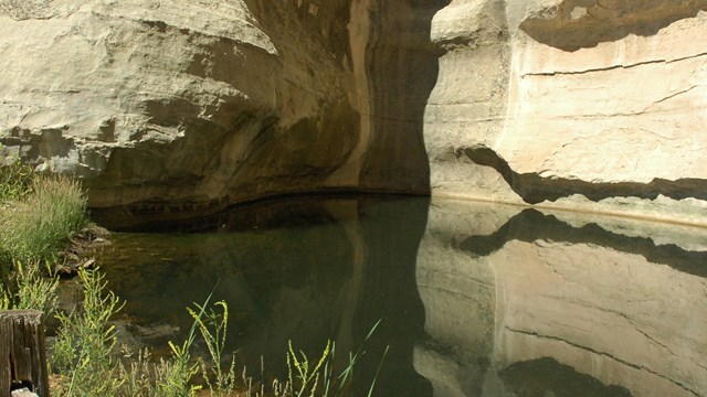 a pool of water at the base of a rock cliff