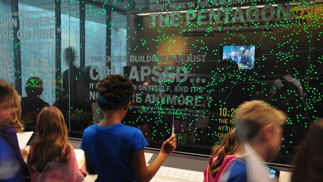 Students standing in front of exhibit with dots indicating the plane over the United States.