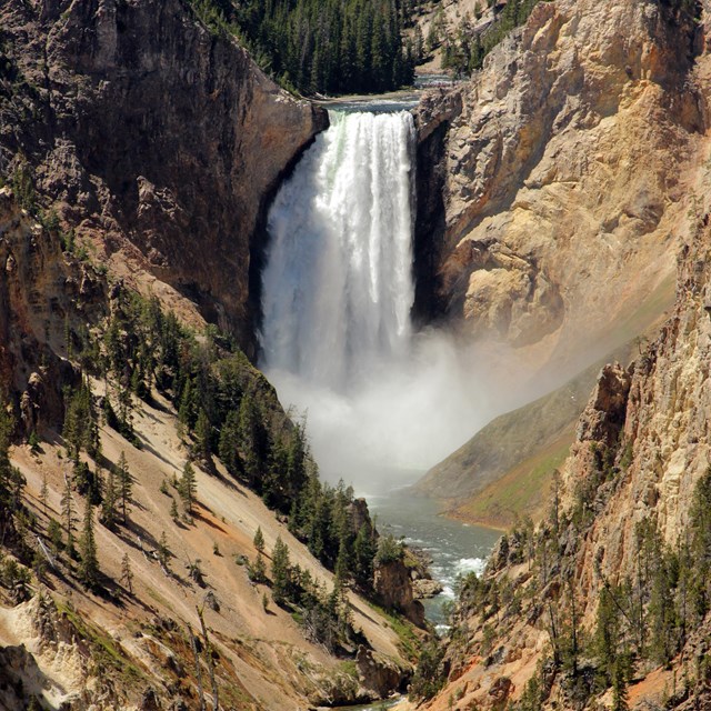 A waterfall crashes down into a tan canyon and the river curves towards the viewer.