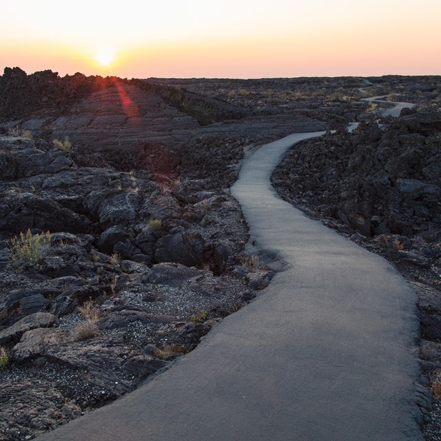 A path leads between lava flows to the setting sun.
