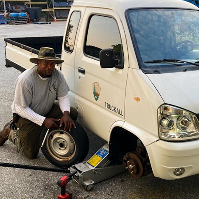 NPS employee next to vehicle while he changes the tire