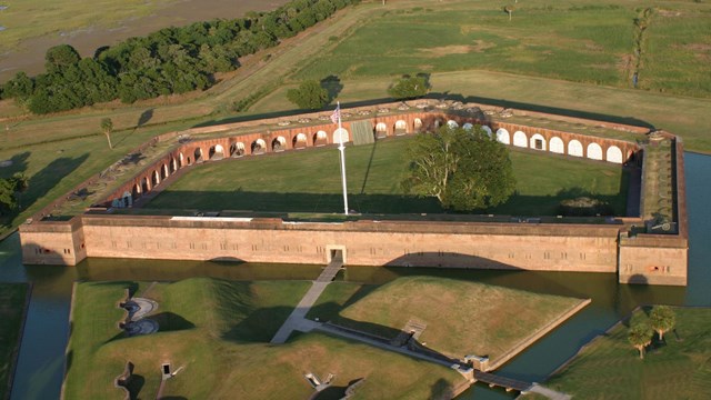An arial view of a 5-sided brick fort with a moat surrounding it. 